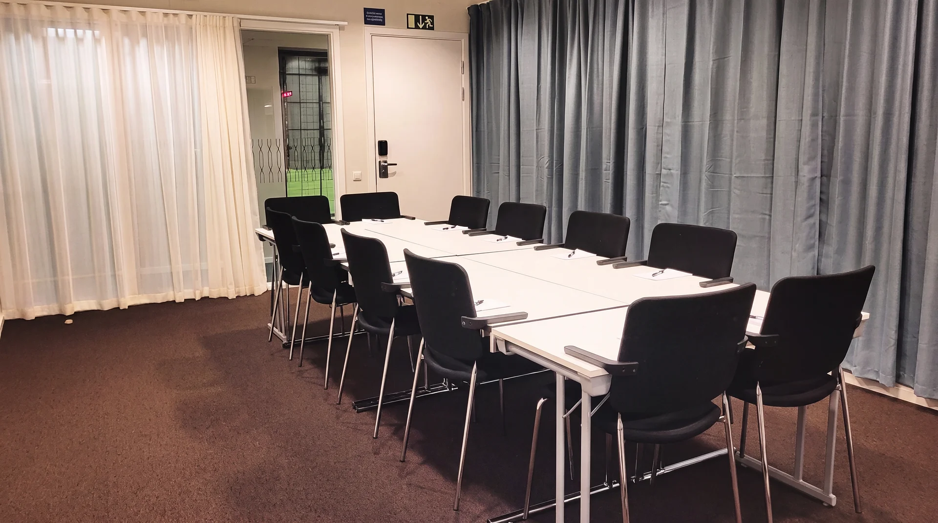 Konferensrum med långt vitt bord och svarta stolar runt om.